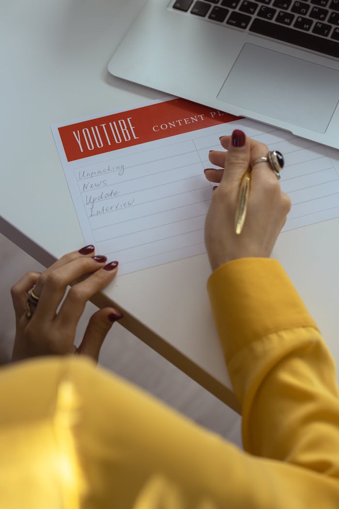 Contact Woman with manicured nails writes YouTube content ideas in office setting.