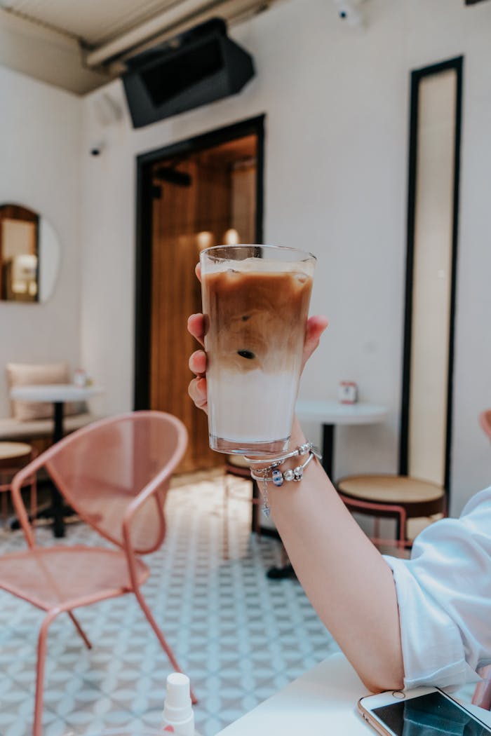 An iced coffee is held aloft in a stylish cafe setting, capturing a trendy lifestyle moment.